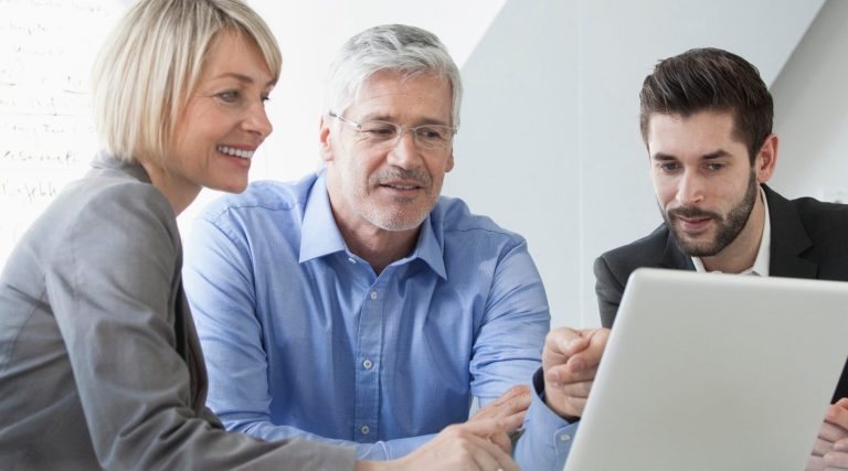 Trois professionnels discutent autour d'un ordinateur portable en souriant.